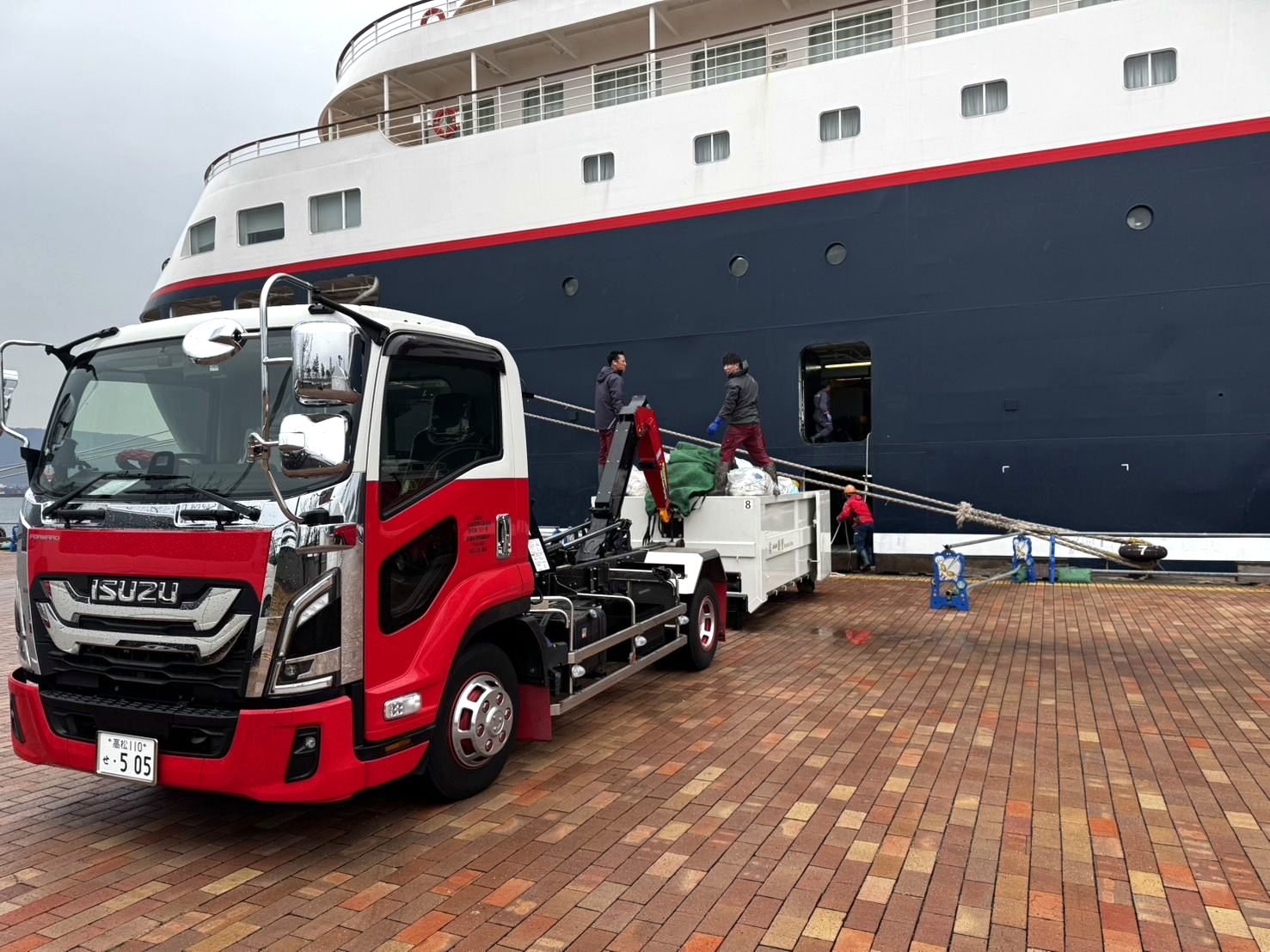 クルーズ客船のそばで廃棄物を回収する勝寳のアームロール車
